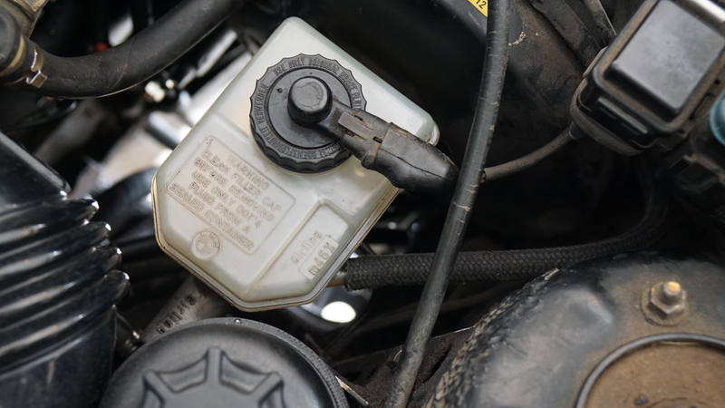 A cleaned up brake fluid reservoir filled with fresh fluid. Note the new clutch master cylinder feed hose coming off the right side of the reservoir.